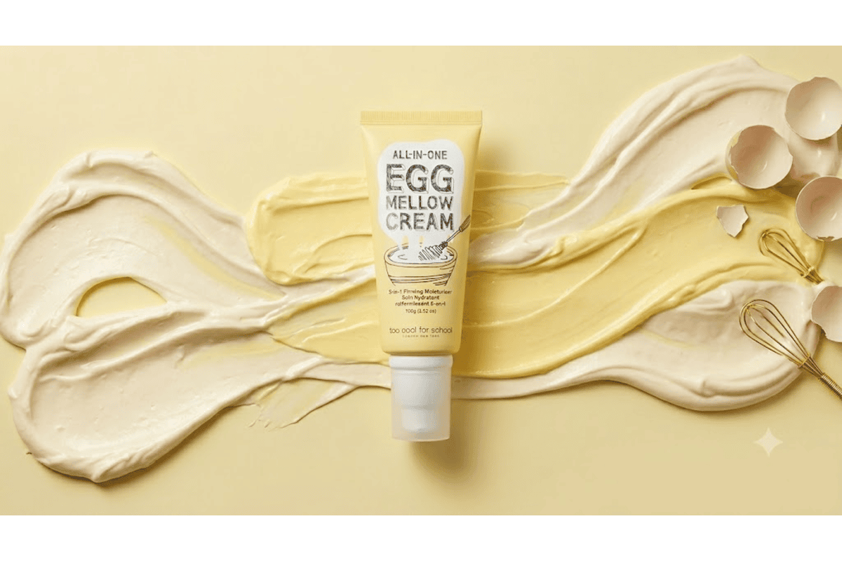 Too Cool For School All-in-One Egg Mellow Cream tube 100 g crème raffermissante 5-en-1 à 98% fibres de collagène et extrait de jaune d'œuf sur fond jaune avec coquilles d'œufs et fouet doré