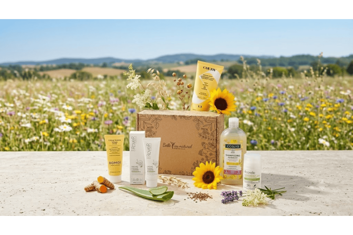 Box beauté bio Belle au Naturel juillet 2026 avec Royer Cosmétique crème visage bave escargot, Bomoï crème solaire visage SPF 30, Cultiv crème corps nourrissante, Coslys shampooing huile cameline, Acorelle déodorant 24h fraîcheur intense reine des prés, présentés dans un champ de fleurs été