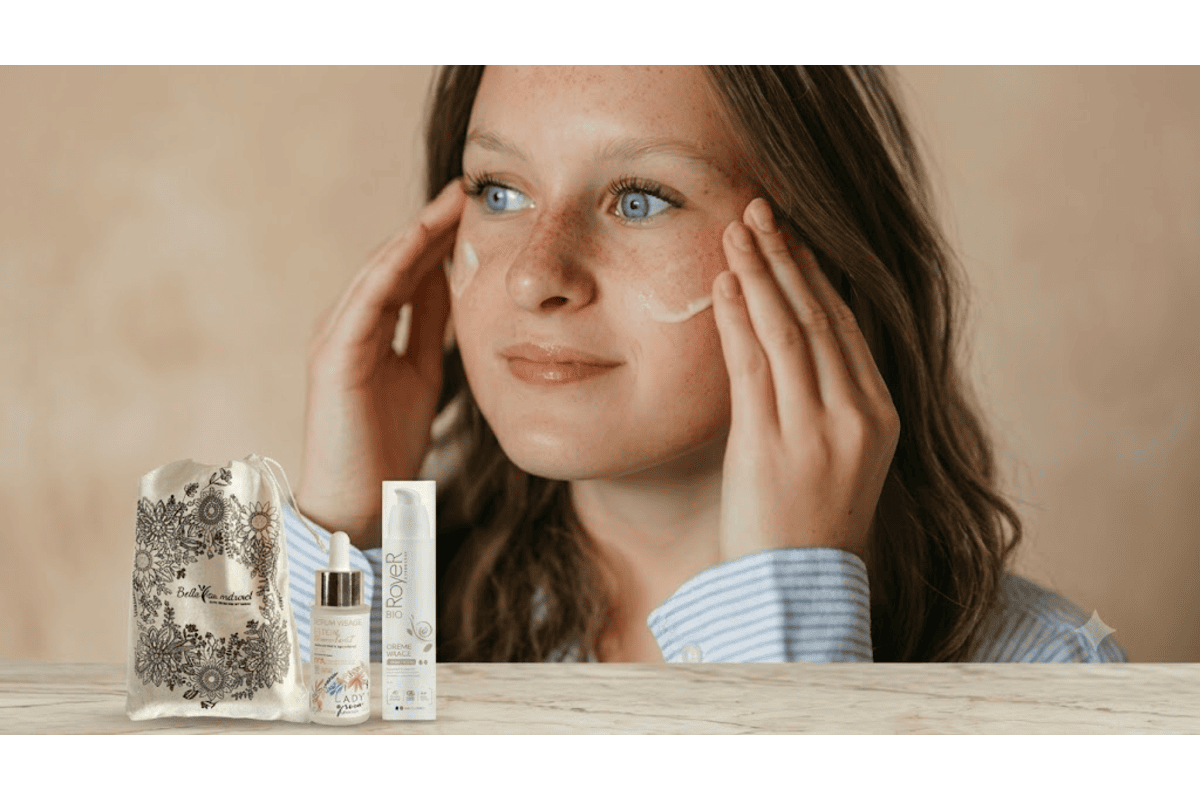 Belle au Naturel Duo Skin Minimalism Booster d'Éclat Bio jeune femme yeux bleus taches de rousseur applique soin éclat sur ses joues chemise rayée bleu serum Lady Green Élixir crème Royer Bio visage pochon coton sigle Belle au Naturel sur table bois fond beige naturel
