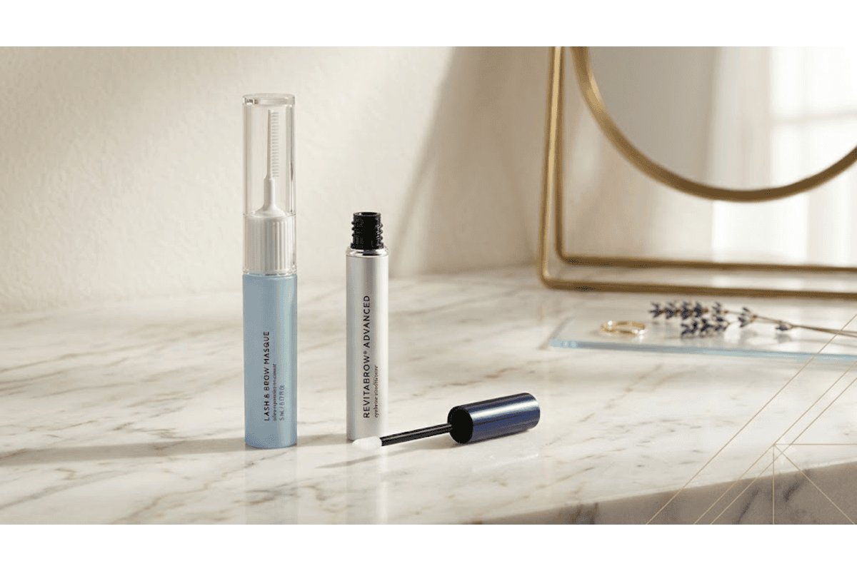 Duo RevitaLash Masque Lash & Brow et Sérum RevitaBrow Advanced posés sur un comptoir en marbre blanc avec miroir doré et brins de lavande, ambiance salle de bain élégante