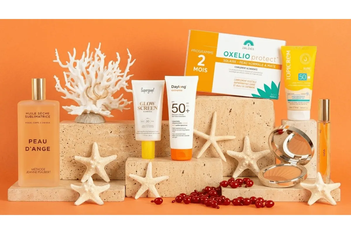 Box Marie Claire Beauté Solaire édition limitée 8 produits accessoire huile sèche Peau d'Ange Méthode Jeanne Piaubert base Supergoop Glow Screen SPF30 lait solaire Daylong SPF50 plus compléments Jaldes Oxelio Protect crème Topicrem SPF50 poudre bronzante Clarins eau de parfum Gas Bijoux La Route des Plages boucles d'oreilles dorées Nilaï corail blanc étoiles de mer capsules rouges fond orange ambiance plage été