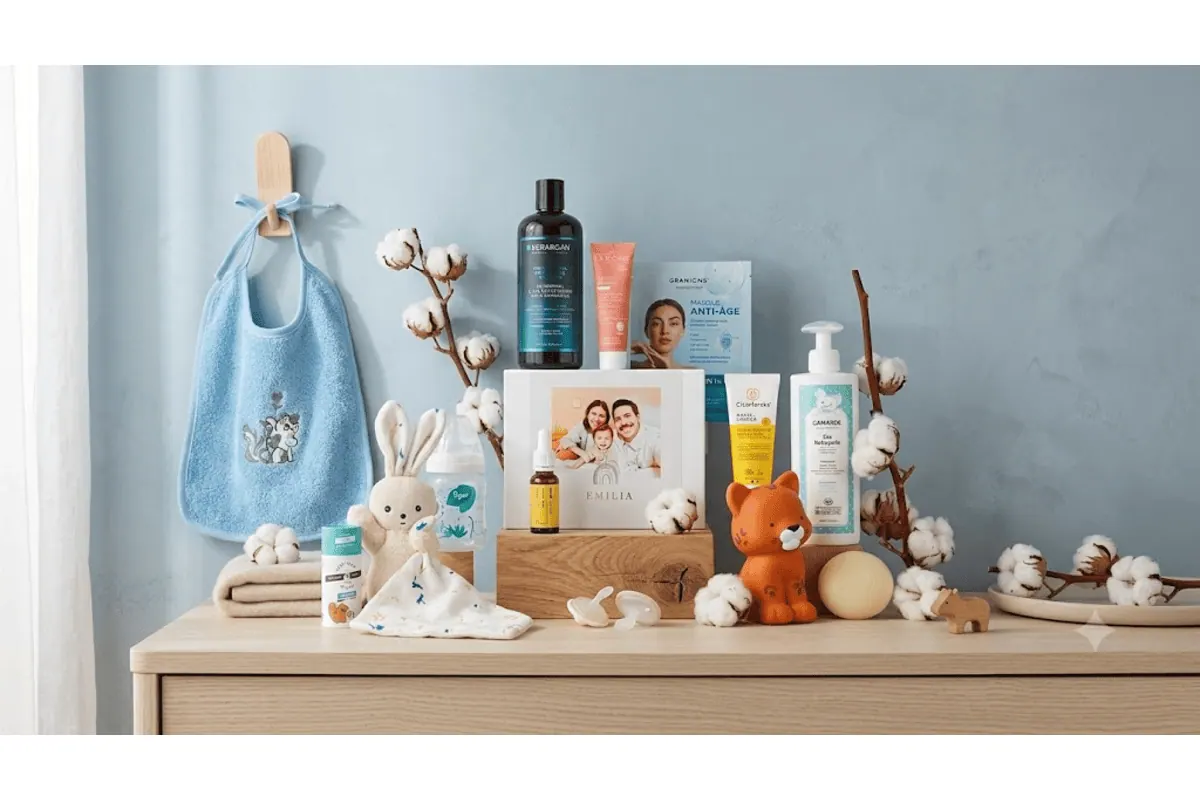 Box magicmaman Bébé Mode d'Emploi avec bavoir chaton bleu Linvosges, doudou lapin KALOO, biberon Tigex, eau nettoyante Gamarde, livre photo Emilia, masques Granions, eau micellaire et déodorant sur commode bleue