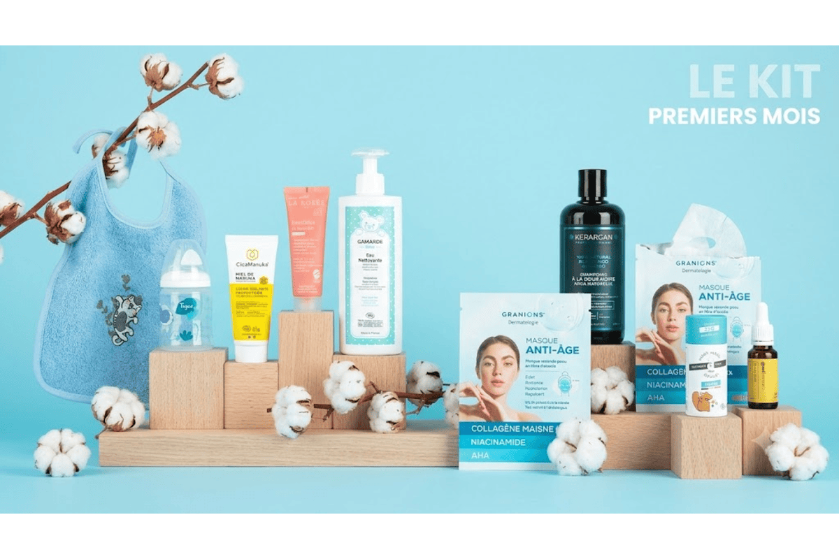 Box magicmaman Bébé Mode d'Emploi avec bavoir Linvosges, biberon Tigex, eau micellaire Gamarde, shampoing Kerargan, masques Granions et déodorant Wash Wash Cousin présentés sur fond bleu doux avec branches de coton