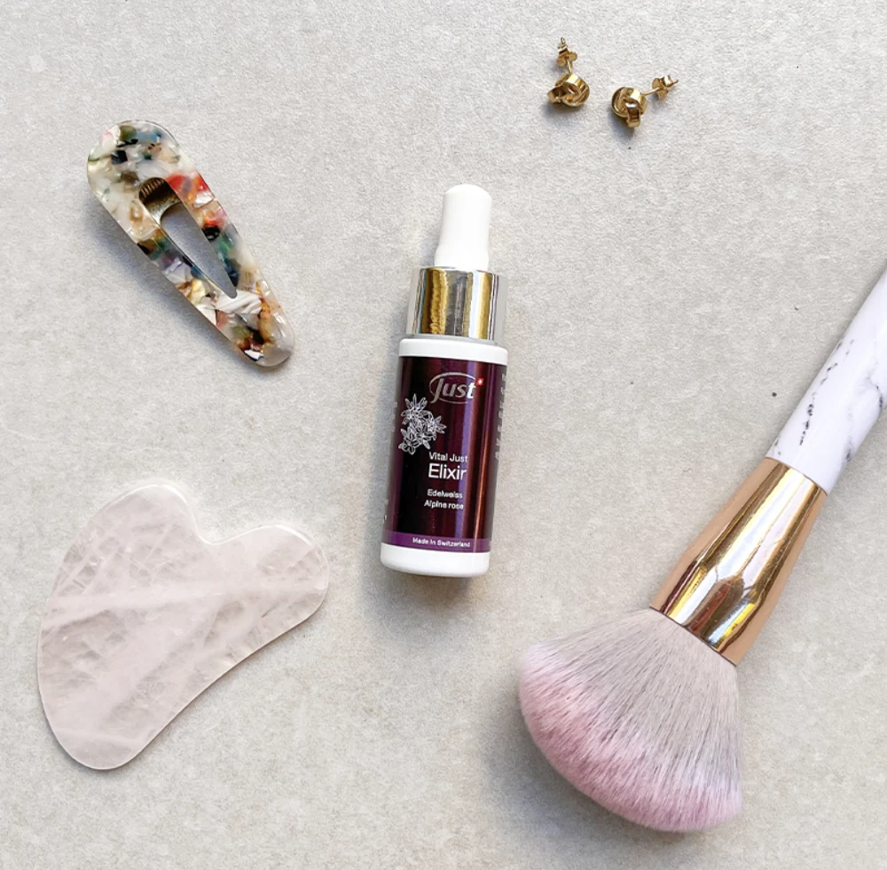 Flacon Vital JUST Elixir aux plantes alpines présenté avec un gua sha et des accessoires de beauté