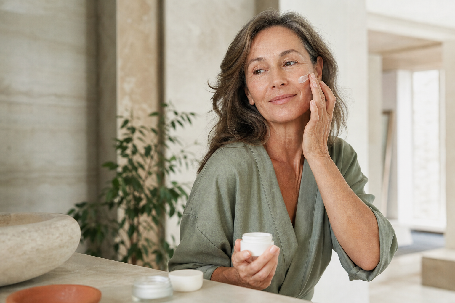 Femme mature appliquant une crème visage dans une salle de bain lumineuse