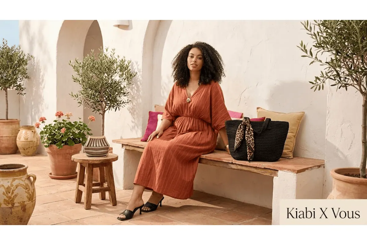 Mannequin grande taille assise sur un banc dans un patio méditerranéen, portant la robe longue Kiabi col croisé avec bijou fantaisie en orange terracotta, avec mention Kiabi X Vous